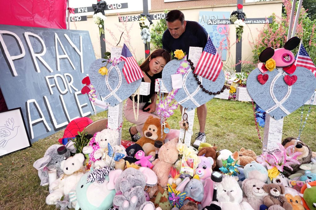 Angela Munoz leaves a message on a cross with the name Cindy Cho as her husband, Rick, looks on at a makeshift memorial at the Allen Premium Outlets, north of Dallas.