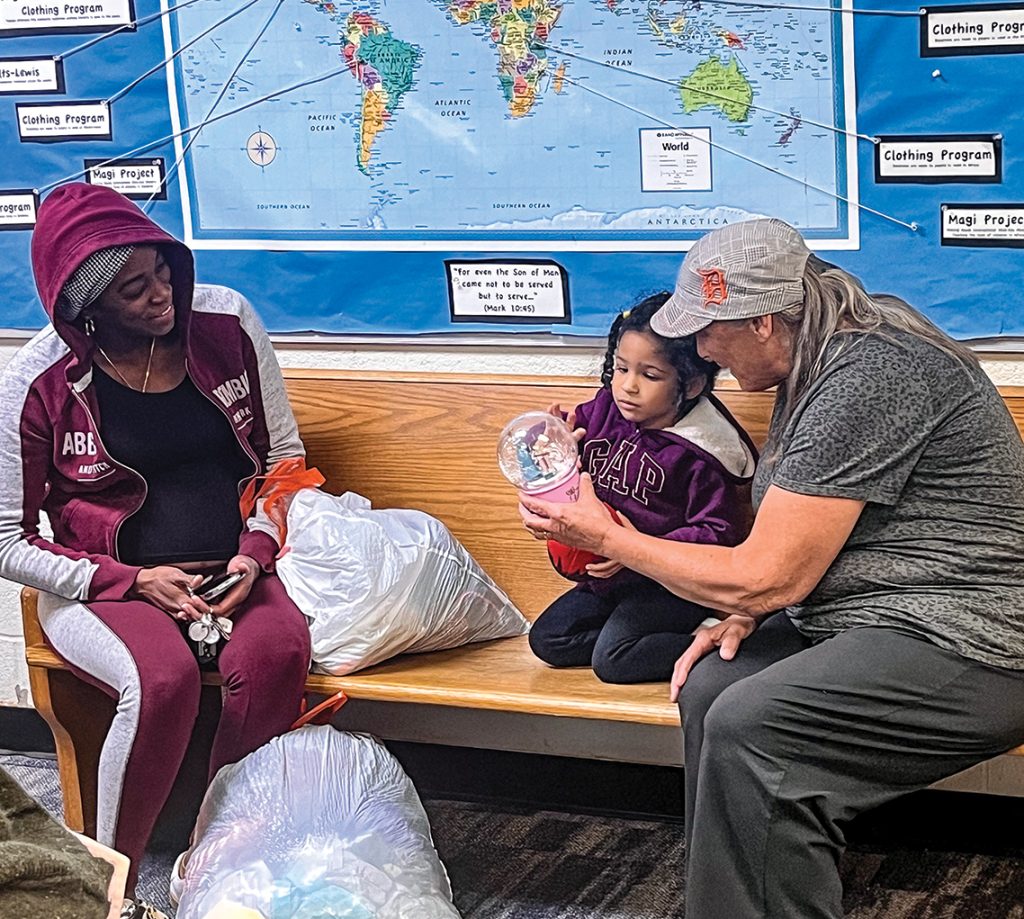 Sandy Simmons hands a Christmas snow globe to a shopper’s child. The world map behind them details the church’s global mission efforts.