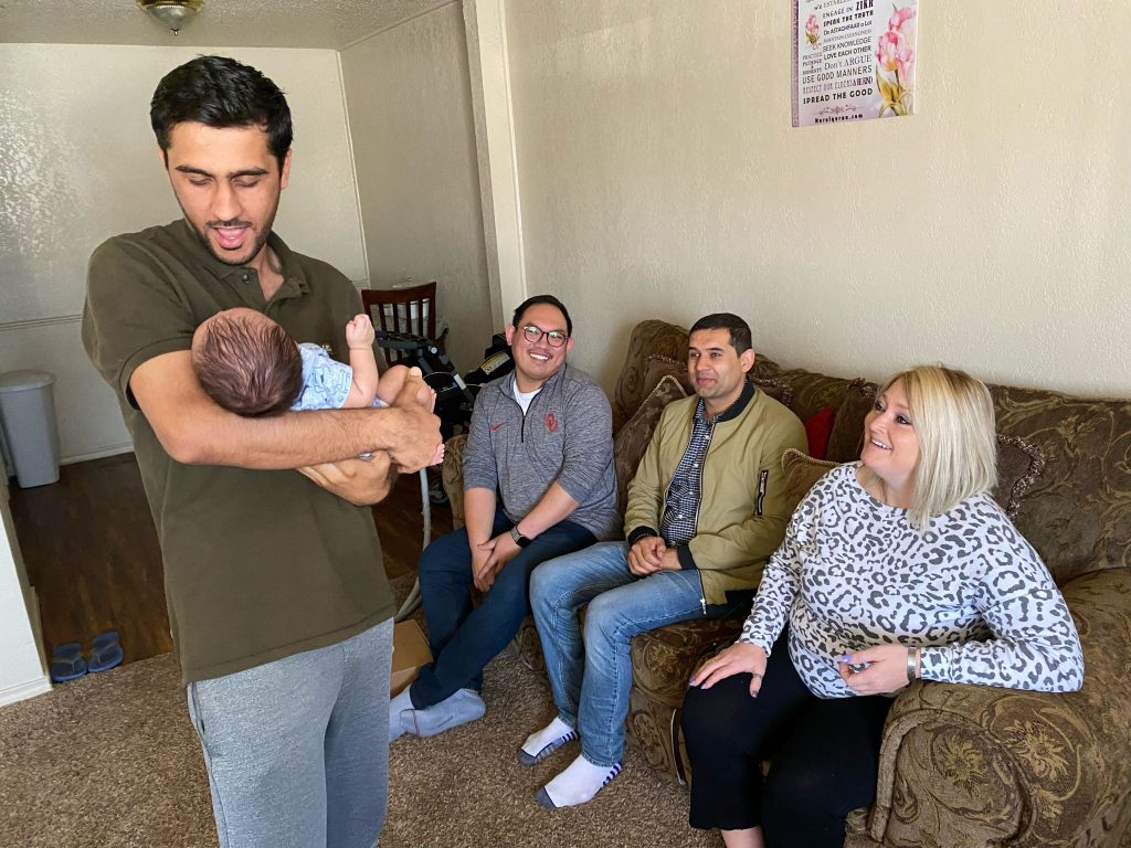 Afghan refugee Shirkhan Nejat, left, talks to his 2-month-old son, Ansar, at the family's Oklahoma City apartment in April 2022. In the background are Joseph Pham, left, a refugee case manager for Catholic Charities of Oklahoma City; a translator, center; and Carly Akard, director of communications for Catholic Charities.