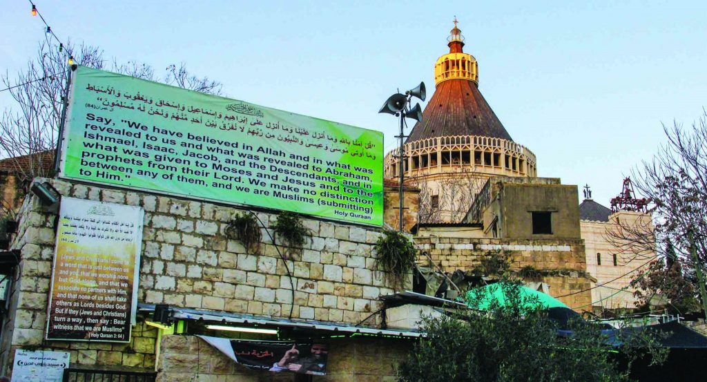 In the city of Nazareth, a billboard bearing a verse from the Quran stands near the steeple of the Basilica of the Annunciation.