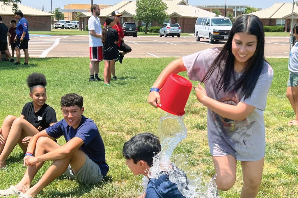 Daniela Martinez dumps a bucket of water over another camper’s head during a modified game of Duck, Duck, Goose at Lubbock Christian University.