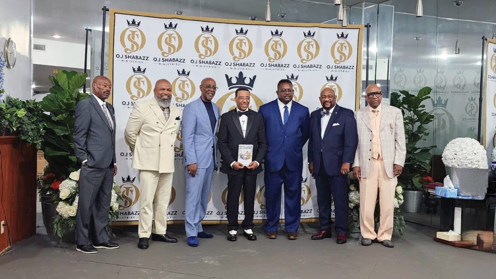 Shabazz, center, displays his book, “Excellence in Ministry: A Guide to Protocols and Etiquette for Church Leaders,” at the publication launch party.