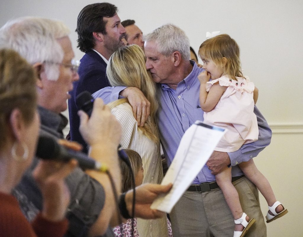 Holding one of his grandchildren, Bill Cosgrove hugs Katie Shields, one of his two daughters, during the memorial service for his wife, Debbie.