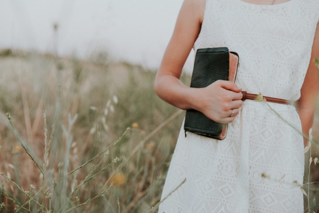 Woman standing in field carrying a Bible in her right hand